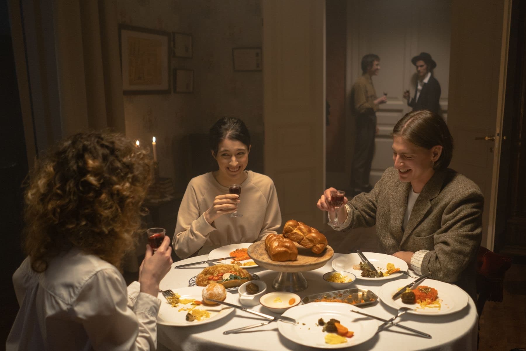 Friends sharing a candlelit Shabbat dinner around a table with challah